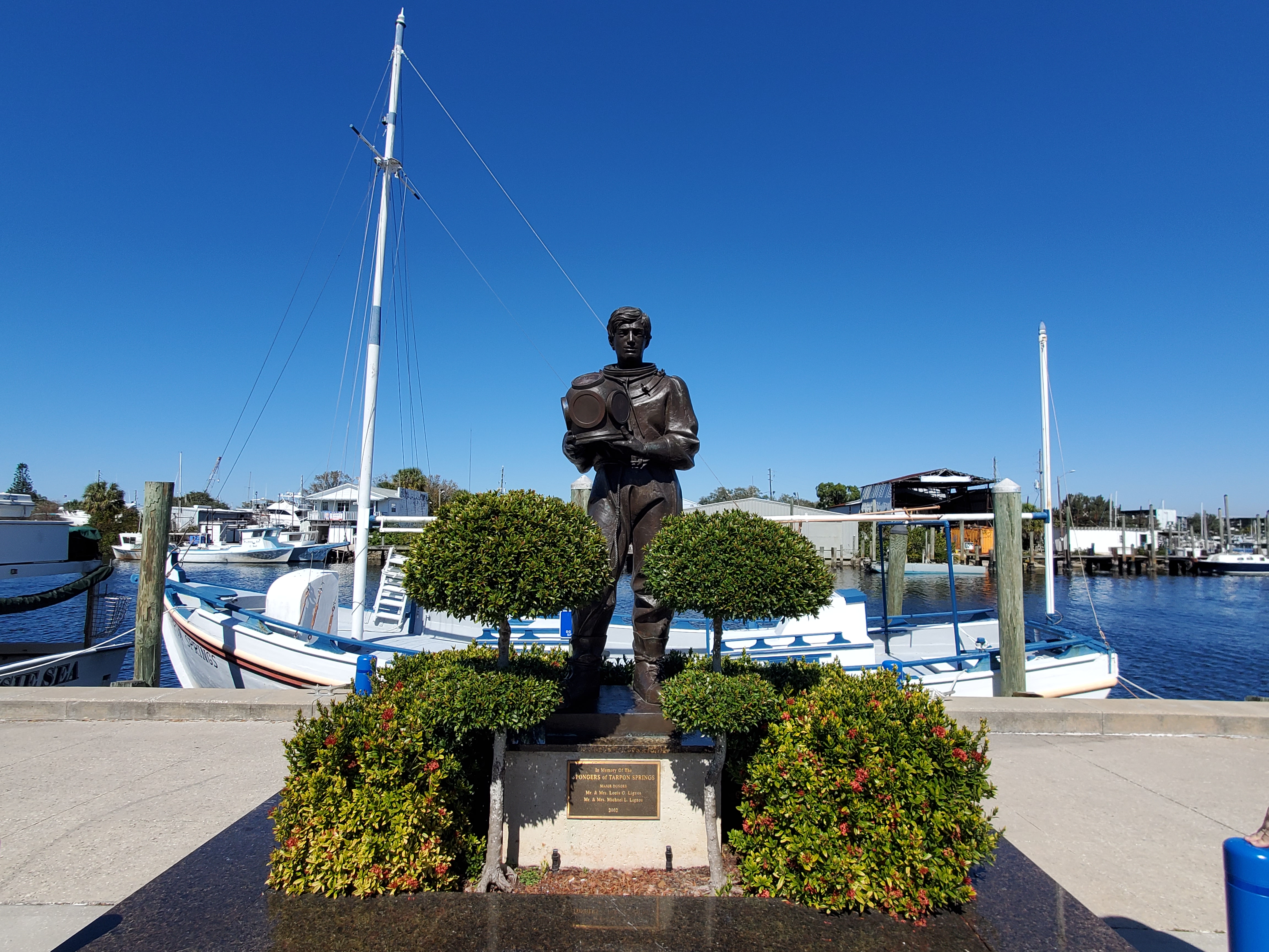 Tarpon Springs Sponge Docks waterfront with boat in the background and statue of diver in the foreground 