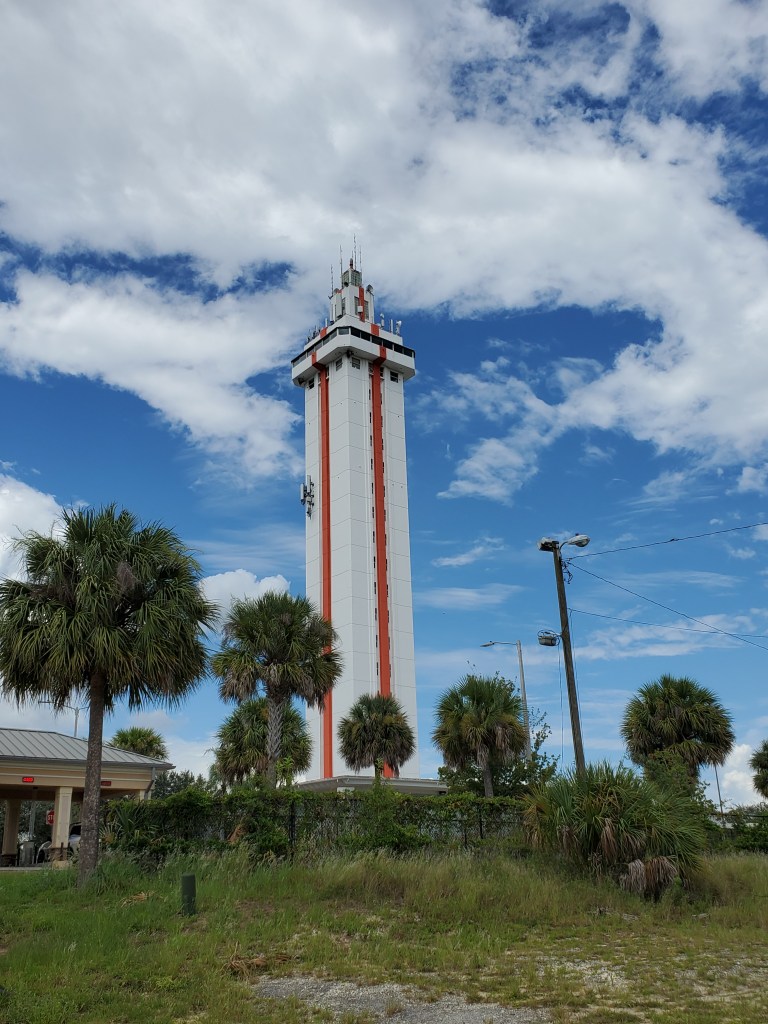 Florida Roadside Attraction, trees in foreground, white tower with orange stripe 
