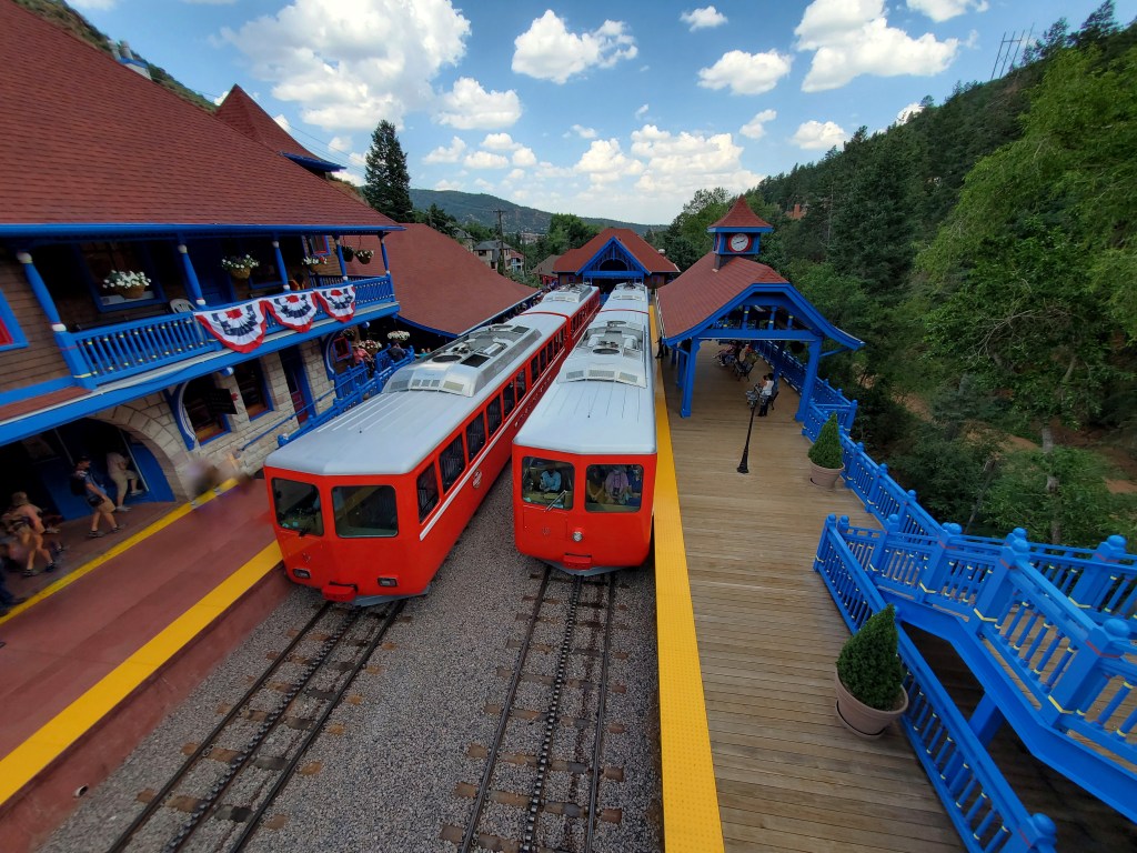 Two red trains sit on train tracks with train platforms along either side