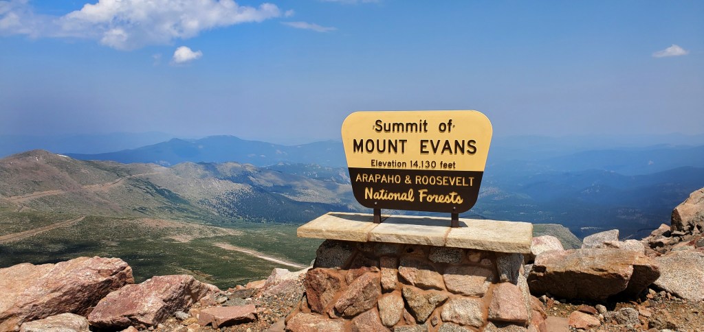 sign of summit of mount evans with mountains in the background 